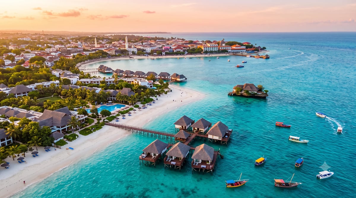 Aerial view of tropical resort with overwater bungalows, white sand beach, turquoise water, and coastal town at sunset