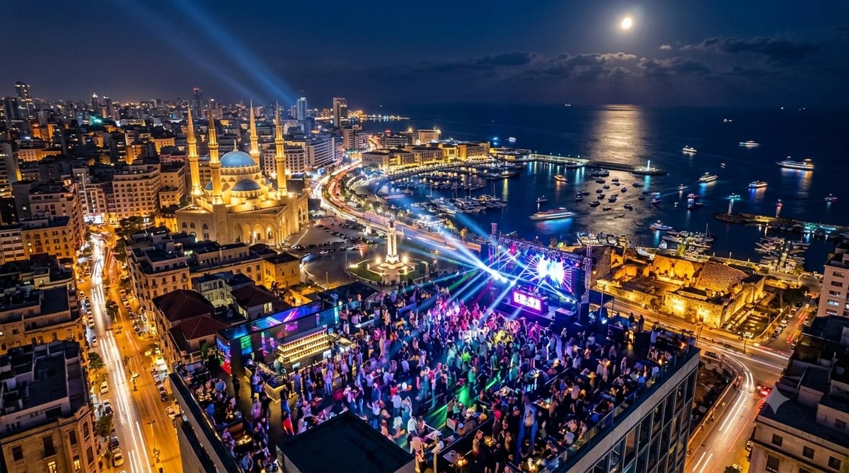 Aerial night view of a vibrant rooftop concert in Beirut with the illuminated Mohammad Al-Amin Mosque, the Beirut Waterfront marina, and the Mediterranean Sea