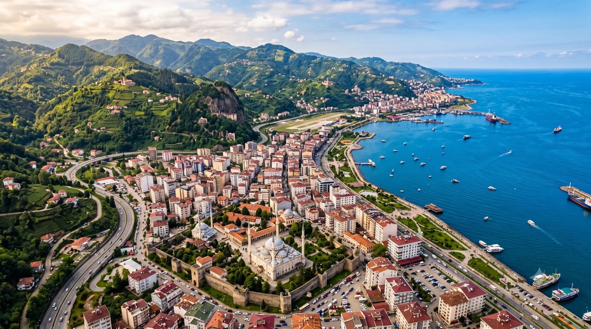 Aerial view of Trabzon's coastal cityscape with Trabzon Castle, the Hagia Sophia mosque, lush green mountains, and the Black Sea harbor