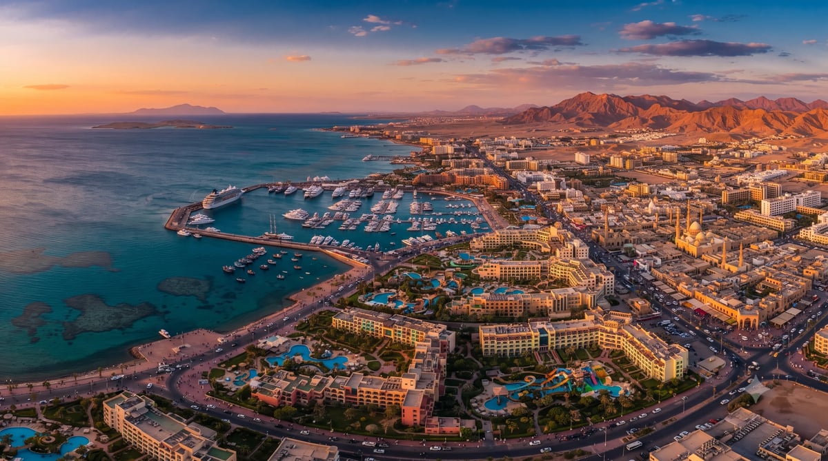 Aerial sunset view of a coastal desert resort town with turquoise waters, beachfront hotels, and mountains in the background