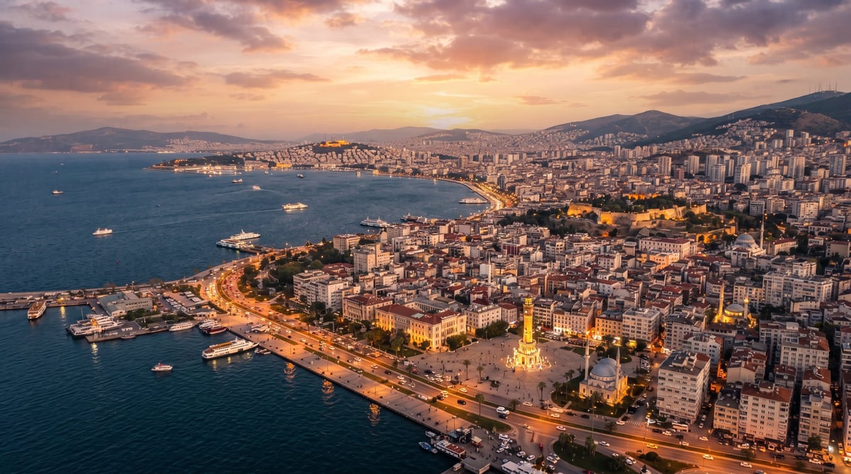 Aerial sunset view of Izmir with the iconic Clock Tower on the waterfront, Konak Square, the Aegean Sea harbor with ships, and the city skyline stretching to the mountains at dusk