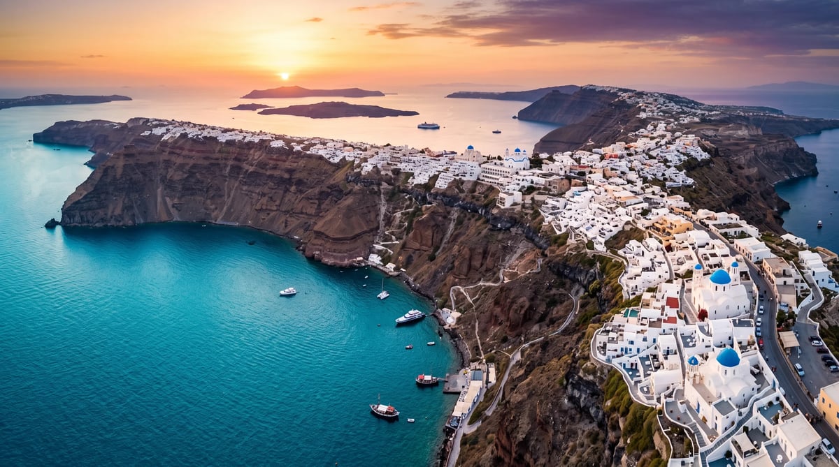 Aerial sunset view of a white-washed clifftop town overlooking turquoise Mediterranean waters with scattered boats