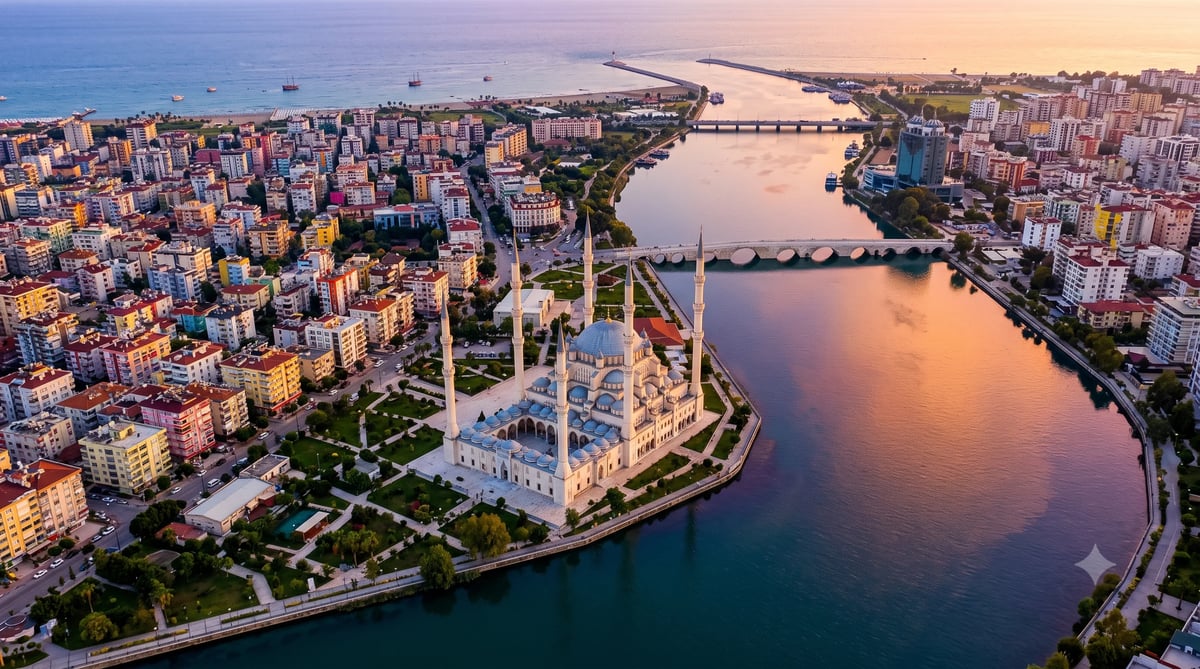 Aerial sunset view of a coastal city with a mosque on a peninsula, surrounding buildings, and waterways at dusk